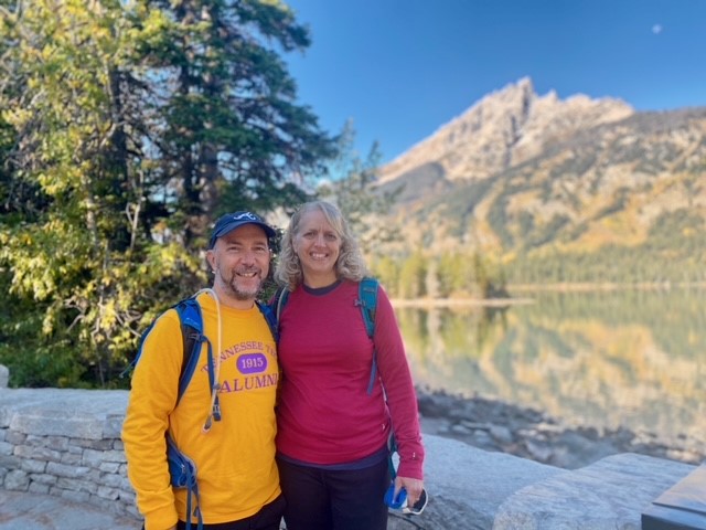 Eric and Angie stand smiling in front of Inspiration Point in Grand Teton National Park.