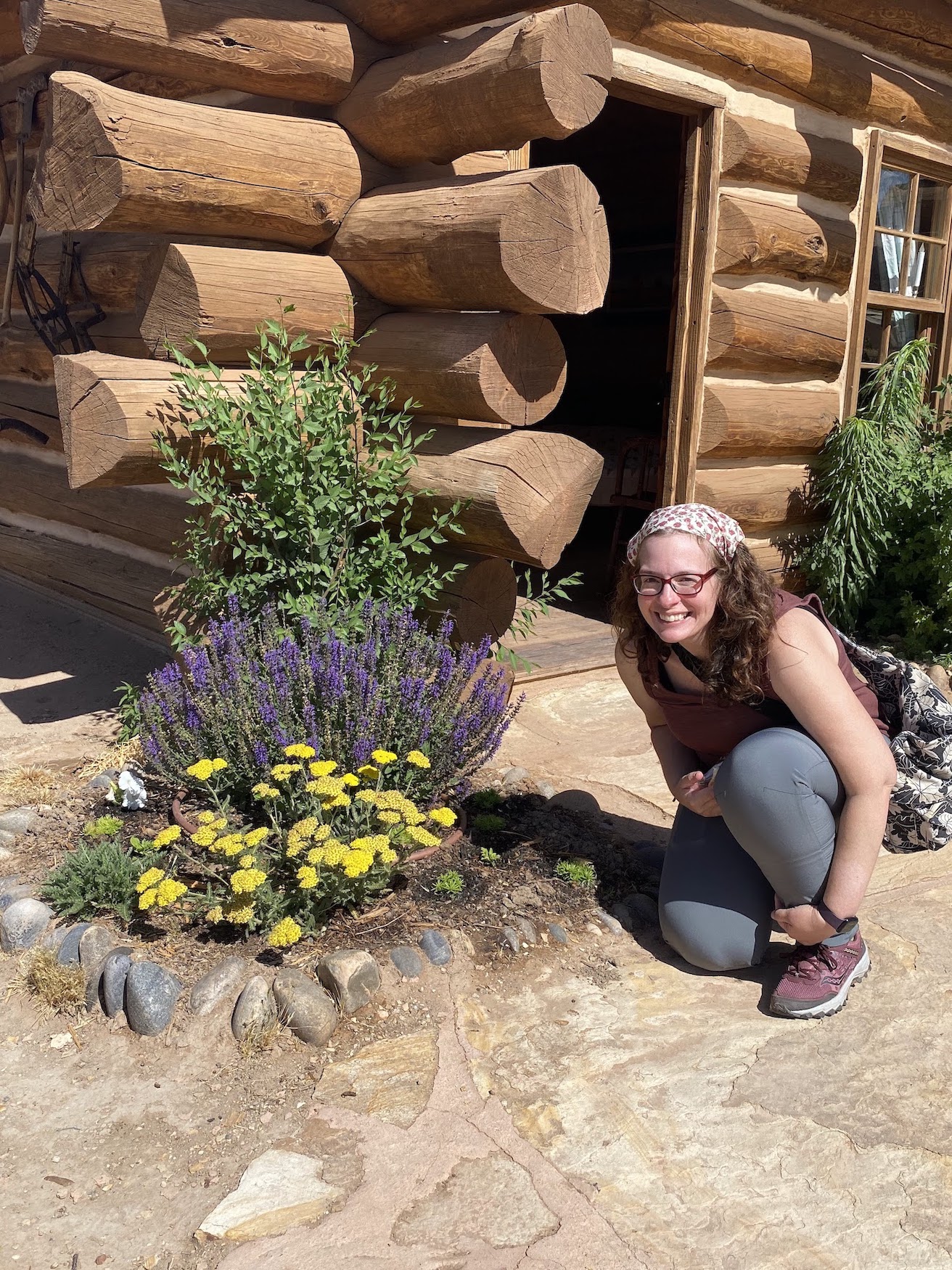 a woman kneels by purple and gold flowers at a Fort along the tour