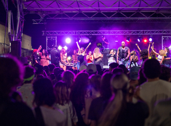 A group of students danging on a music staff with the crowd watching them in the foreground. 