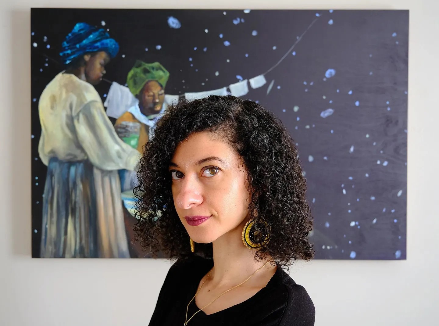 Headshot of Chanda Prescot-Weinstein looking aslant at the camera in front of a painting of black women and stars.
